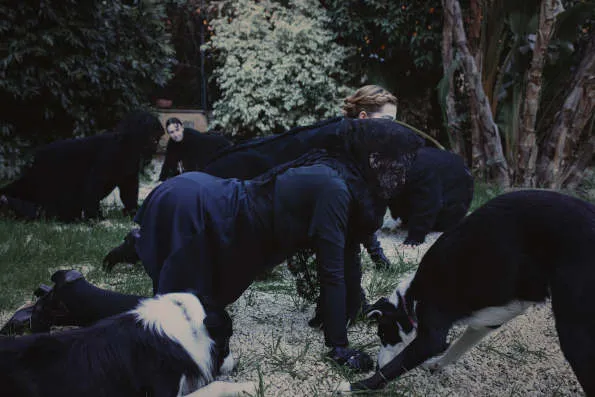 Mujeres vestidas de negro en cuadrupedia junto a perros sobre un bosque