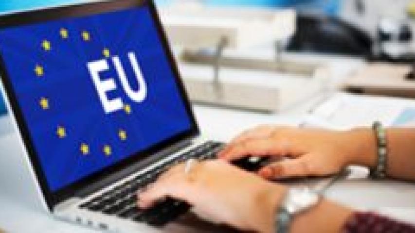 Manos sobre un portátil, donde en la pantalla se muestra la bandera de la UE y las siglas EU