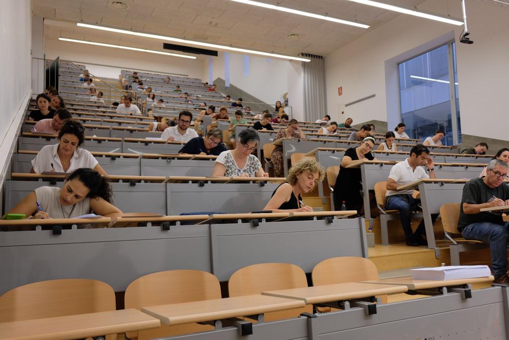 Un grupo de personas sentadas en mesas de un aula en escalera realizando un examen