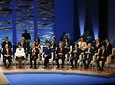 Los consejeros y el portavoz del Gobierno andaluz, sentados en el escenario del Teatro de la Maestranza al comienzo del acto institucional de entrega de medallas.
