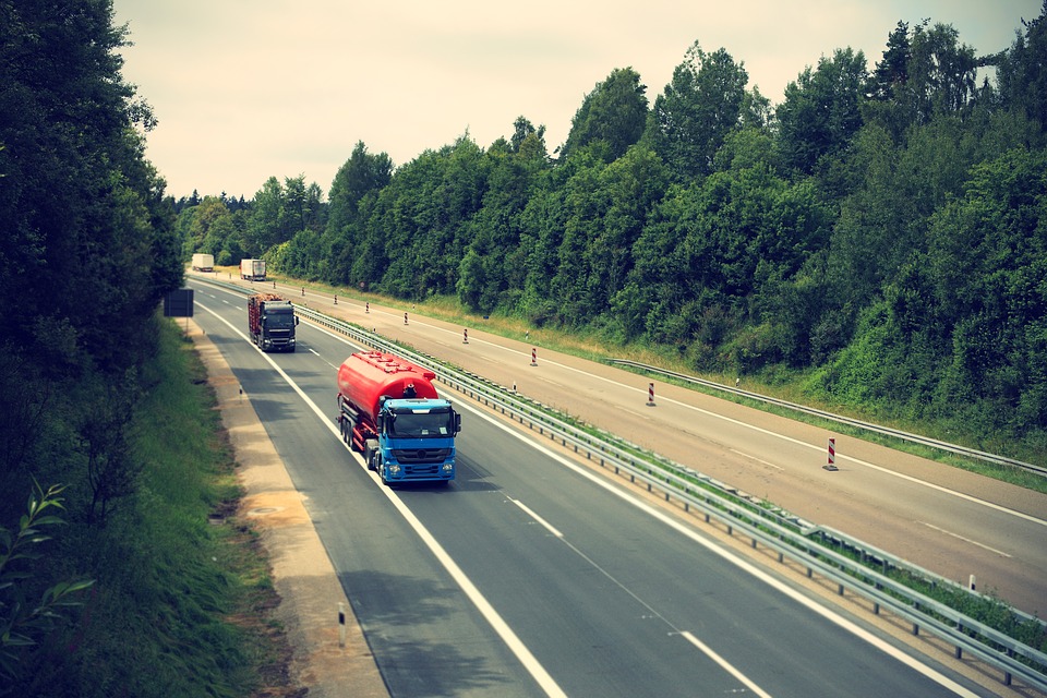 Ampliar imagen: vehículos pesados circulando en una autovía con vegetación frondosa y árboles en sus márgenes.