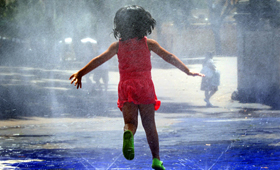 Una niña se refresca en una fuente.