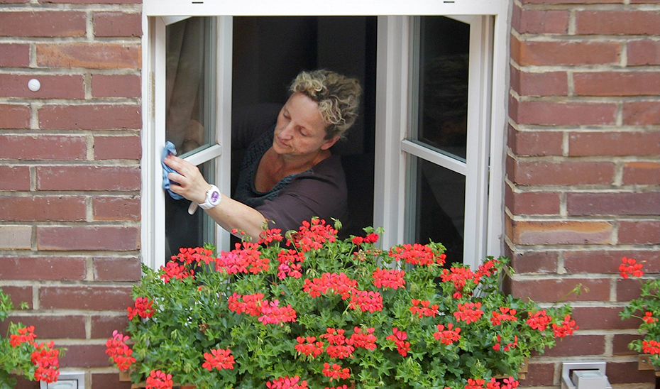 Una mujer limpiando las ventanas de su vivienda.