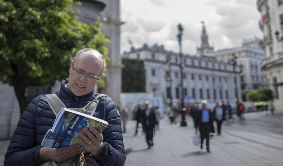 Un turista, en la Plaza Nueva de Sevilla consulta una guía de viaje sobre Andalucía. 