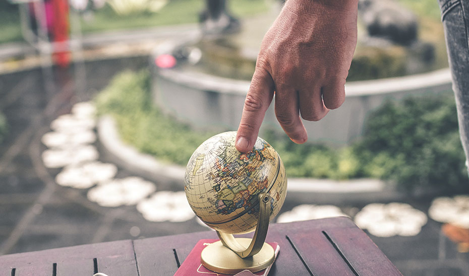 
			      Una persona señala sobre un globo terráqueo.			    
			  
