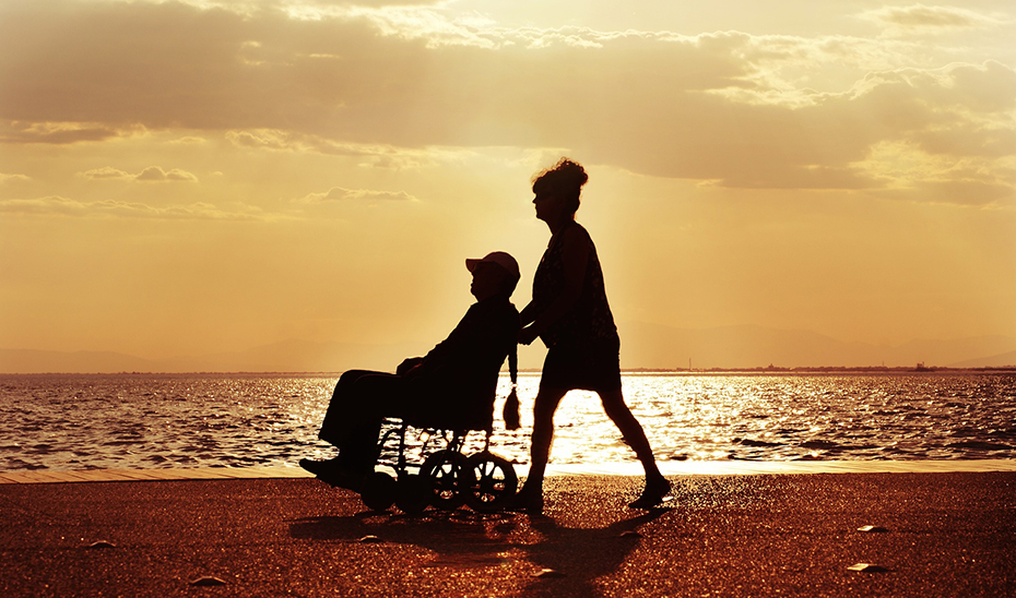 Una mujer empuja una silla de ruedas por una playa.