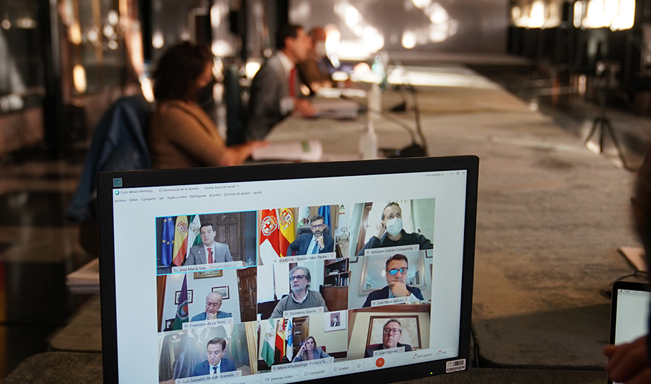 El presidente de la Junta y los alcaldes de las ocho capitales andaluzas, en un monitor durante la reuniíon.