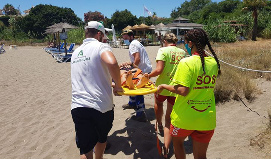 Auxiliares de playa colaboran en la evacuación de una persona atendida por socorristas.