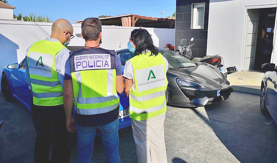 Dos agentes de la Agencia Tributaria Andaluza con un policía, junto a los coches intervenidos.