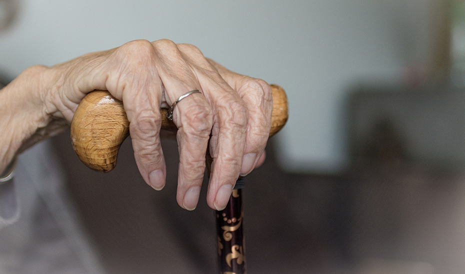 Una persona de avanzada edad apoya su mano en un bastón para poder moverse.