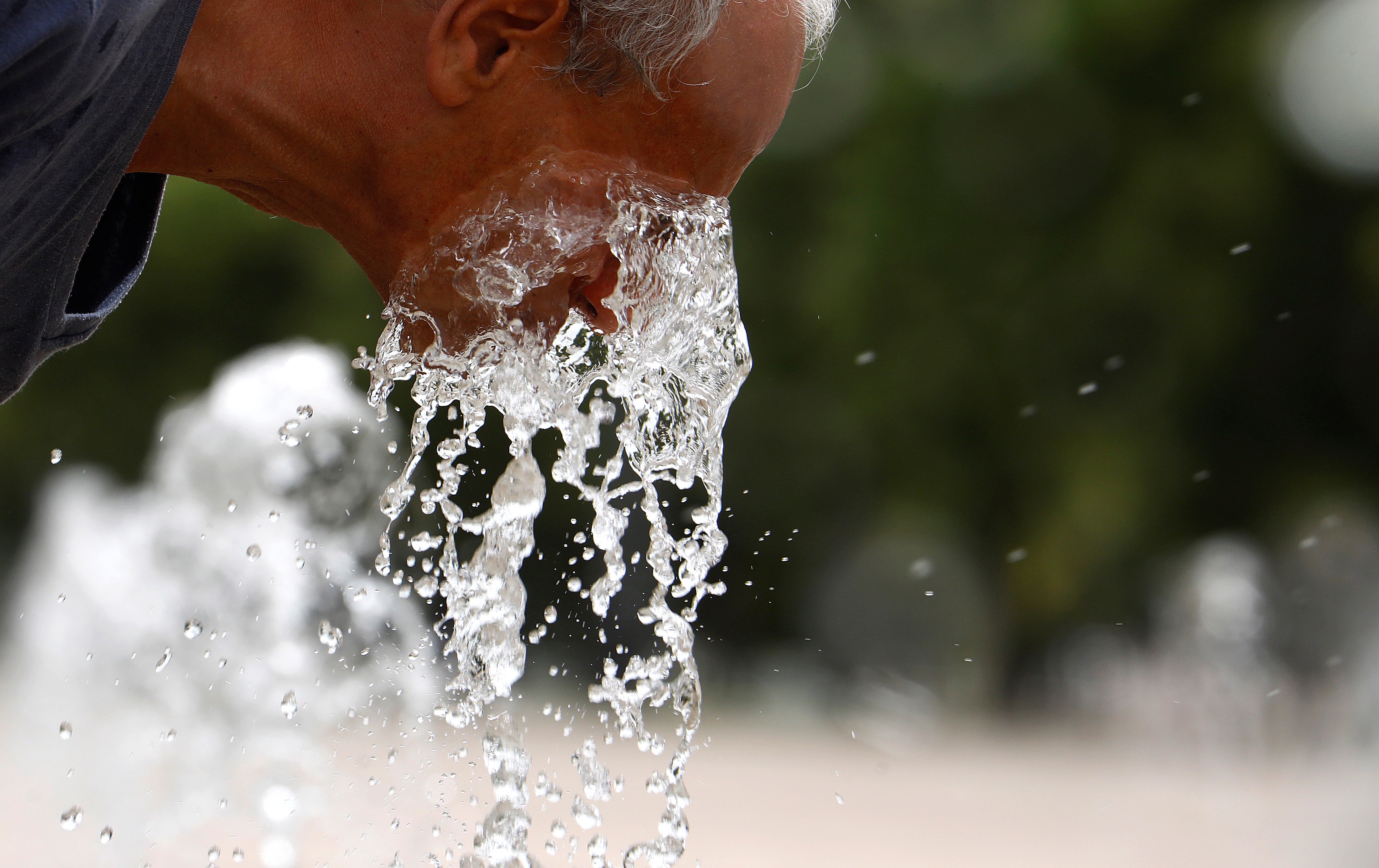 Un hombre se refresca en una fuente.