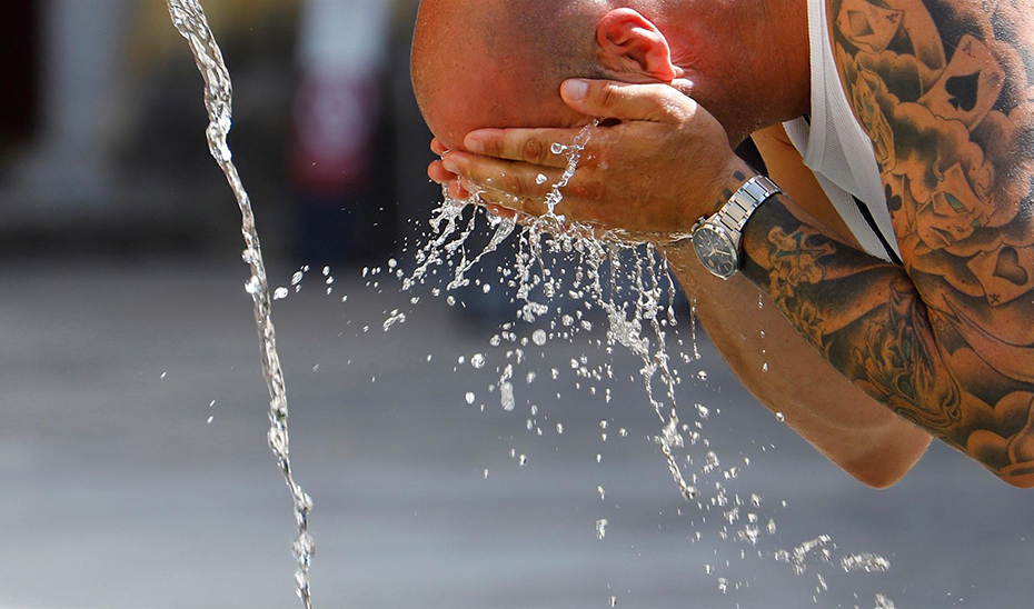Un hombre se refresca en una fuente durante una de las olas de calor del verano.