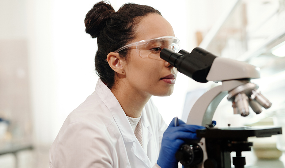 Una investigadora estudia a través del microscopio en un laboratorio.