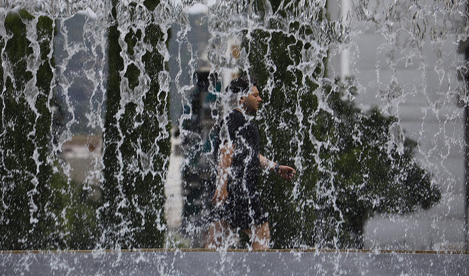 Un hombre pasea tras una cortina de agua de una fuente. 