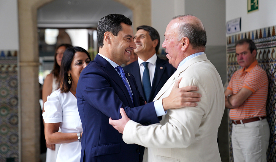 El presidente de la Junta, Juanma Moreno, saluda a Javier Delmás, nieto de Blas Infante, en presencia de la presidenta del Parlamento, Marta Bosquet.