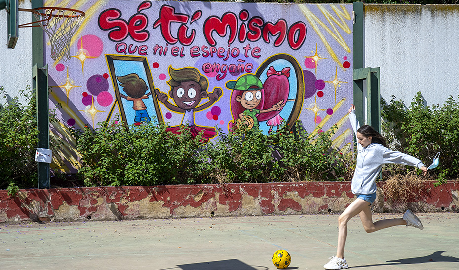 Una joven juega junto a un cartel que fomenta el bienestar emocional en una pista deportiva.
