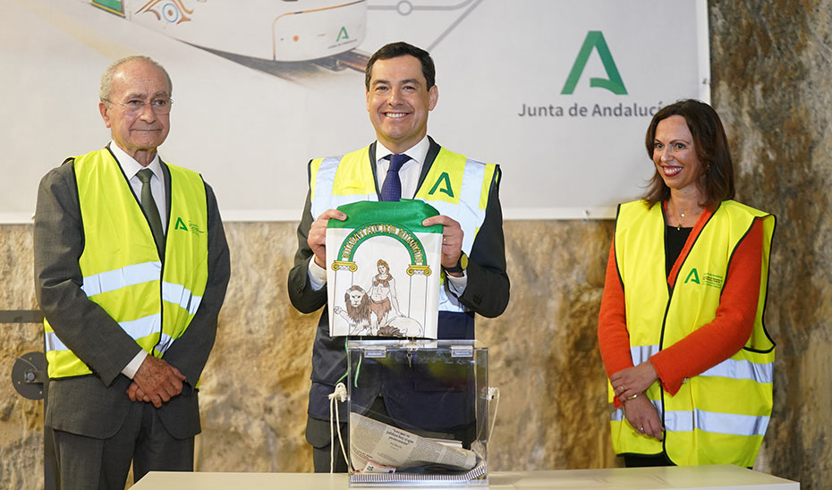 El presidente andaluz, entre el alcalde de Málaga y la consejera de Fomento, muestra la bandera de Andalucía introducida en la urna utilizada para la primera piedra de las obras de ampliación del metro de Málaga.