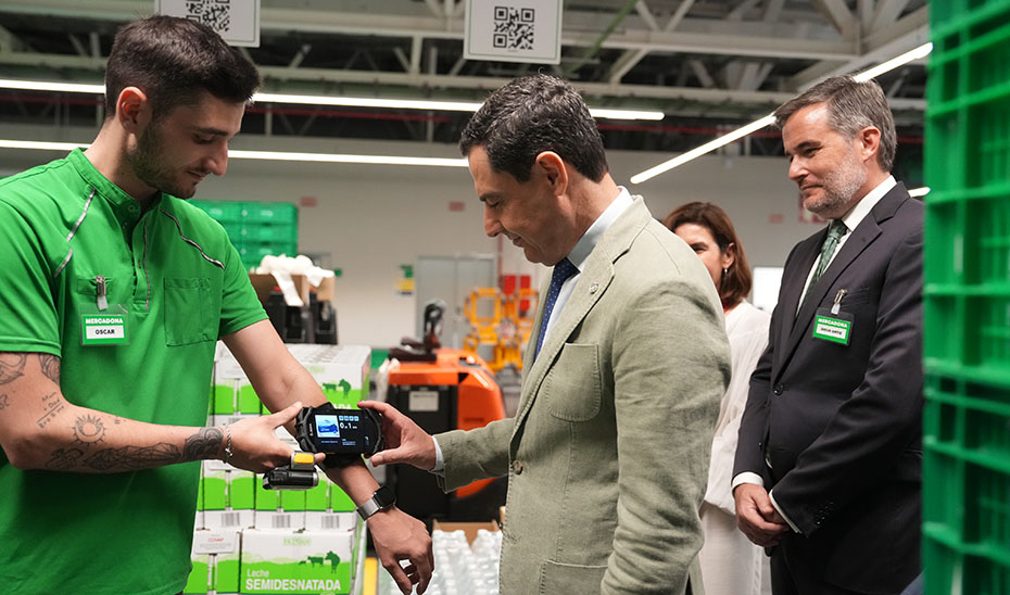 Juanma Moreno observa un dispositivo del nuevo centro logístico de ventas de Mercadona.