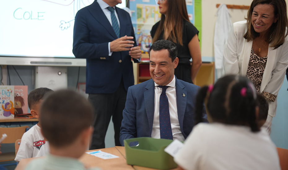 Juanma Moreno sentado en un pupitre con escolares del CEIP Juan Ramón Jiménez de Sevilla.