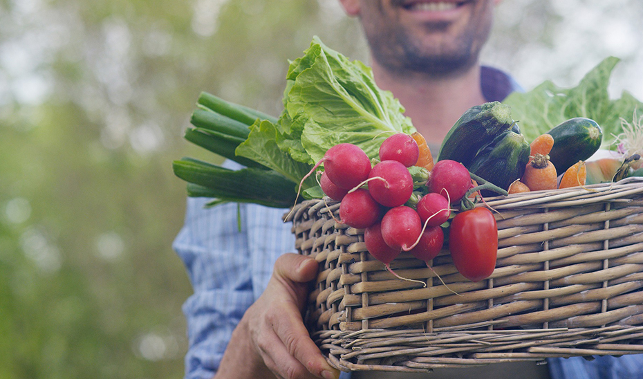Un agricultor porta una cesta con productos ecológicos.