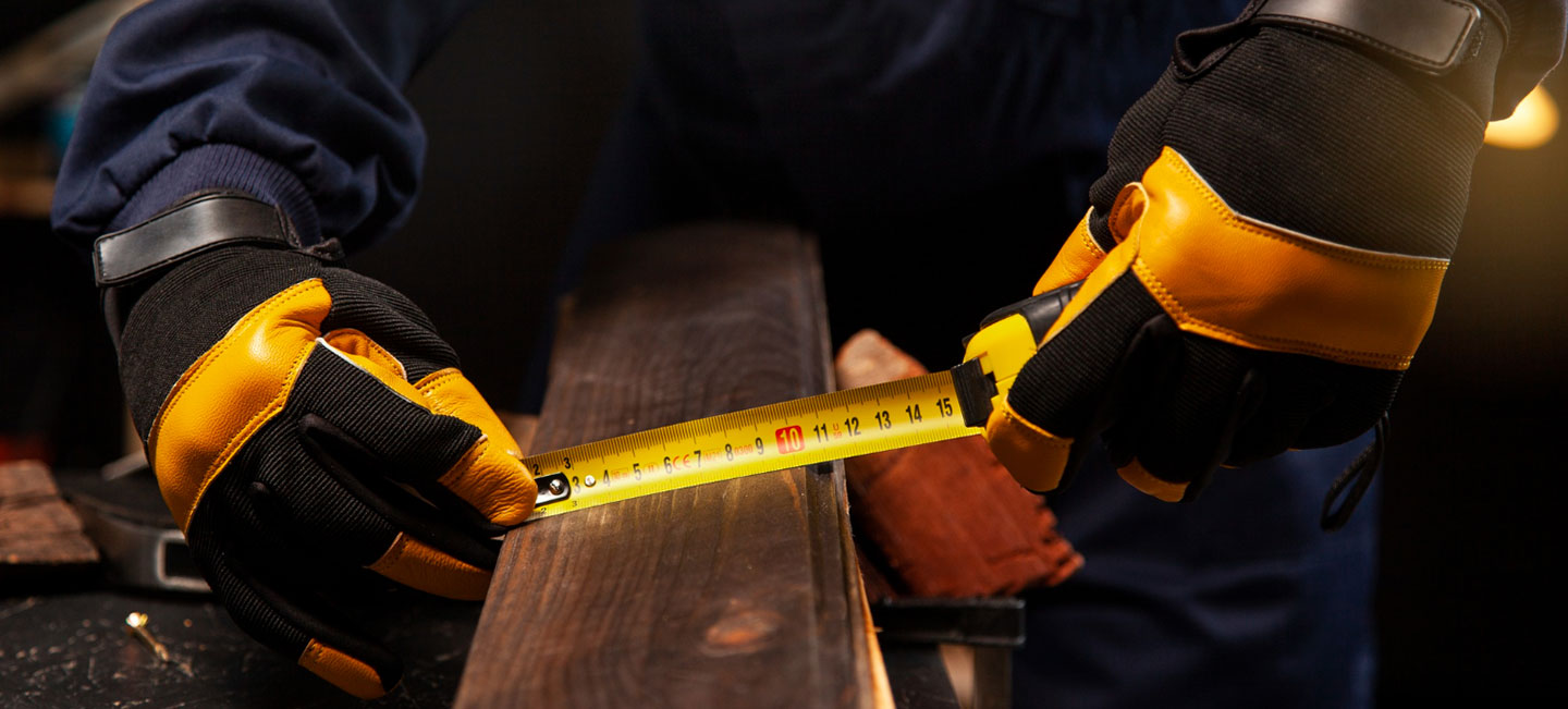 Unas manos con guantes de seguridad miden el ancho de una tabla de madera